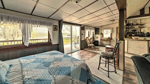 A bedroom with a large bed, a chair, a desk, and a view of the outdoors.