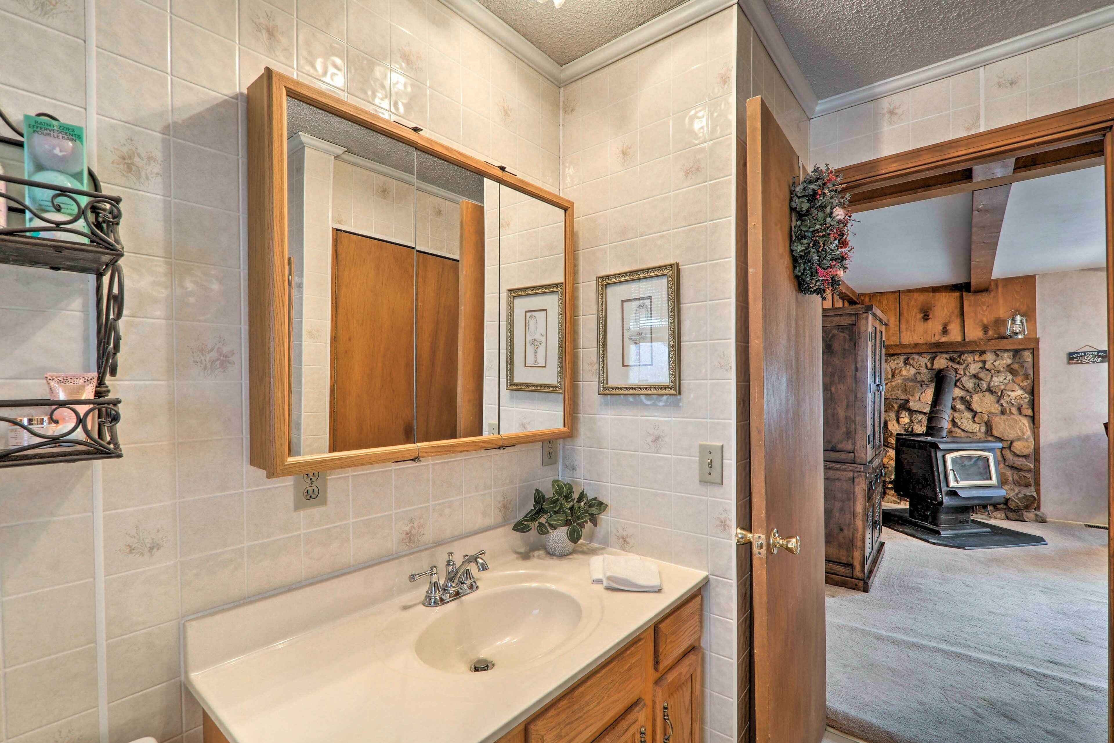 A bathroom with a large mirror, a sink, wooden cabinets, and a stone wall.