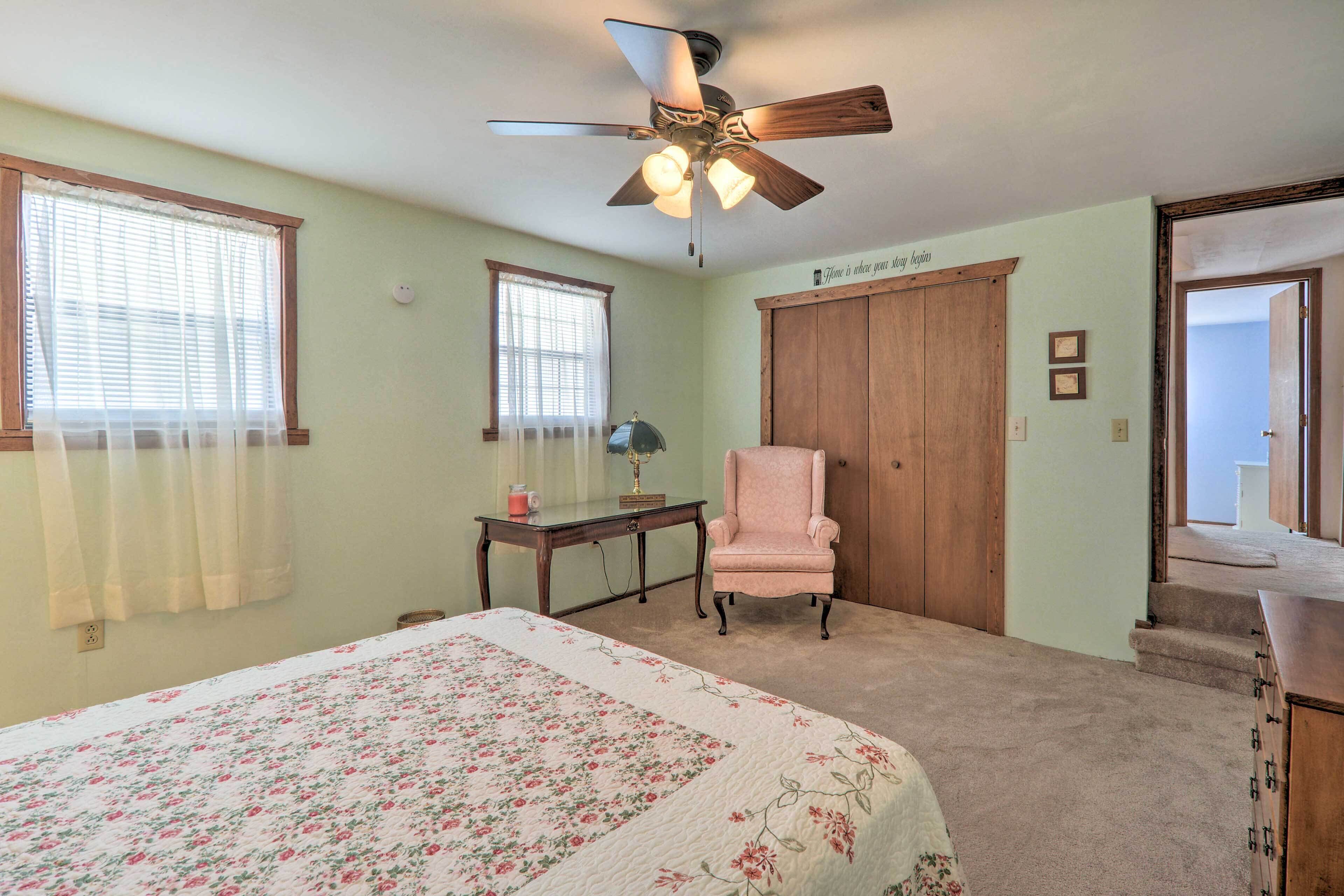 A bedroom with a bed, a desk, a chair, a wardrobe, and a ceiling fan.