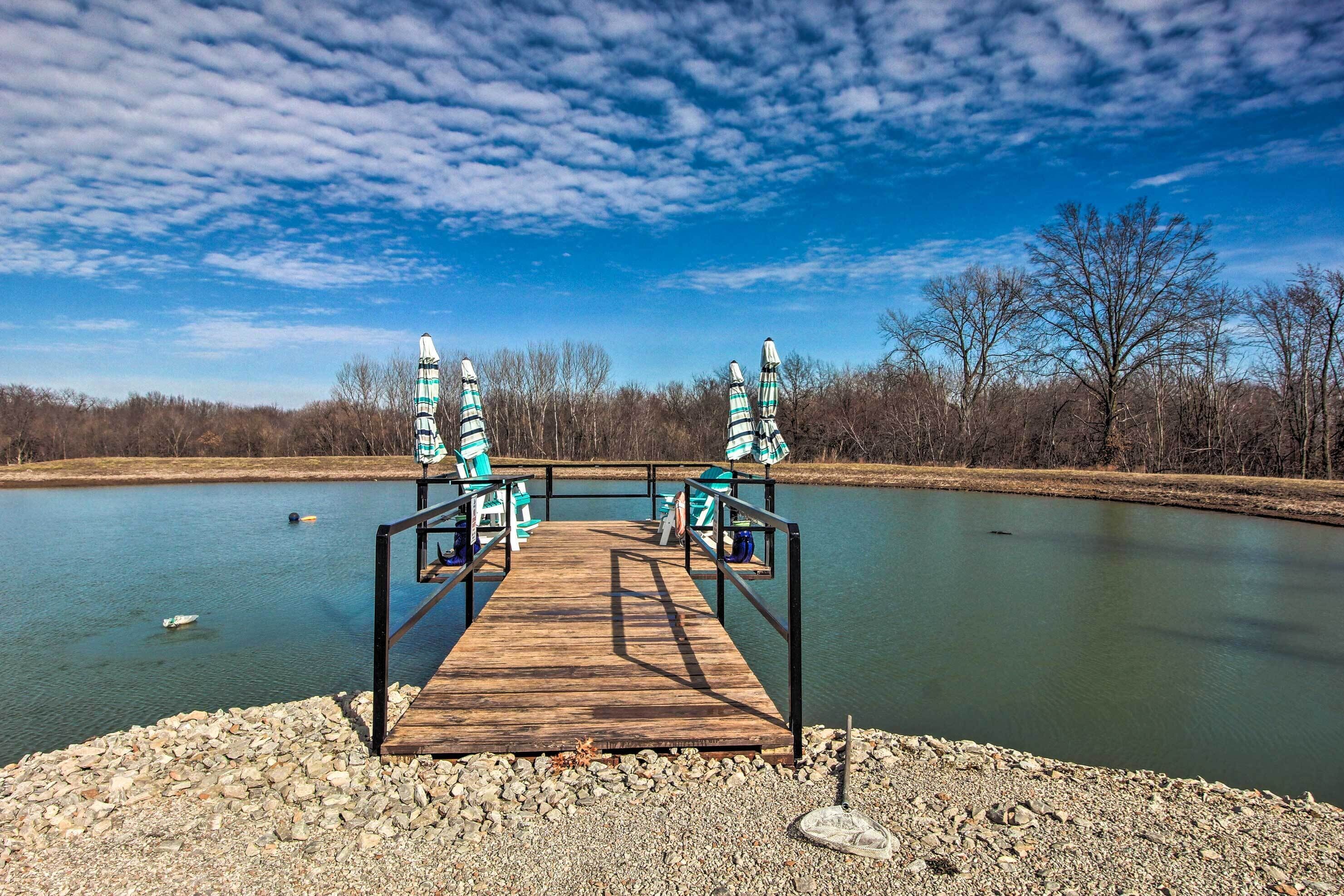 A wooden dock leading to a calm lake with chairs and umbrellas.