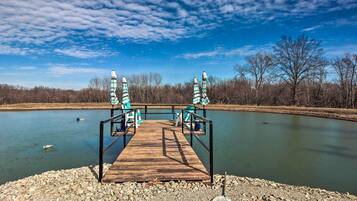 A wooden dock leading to a calm lake with chairs and umbrellas.