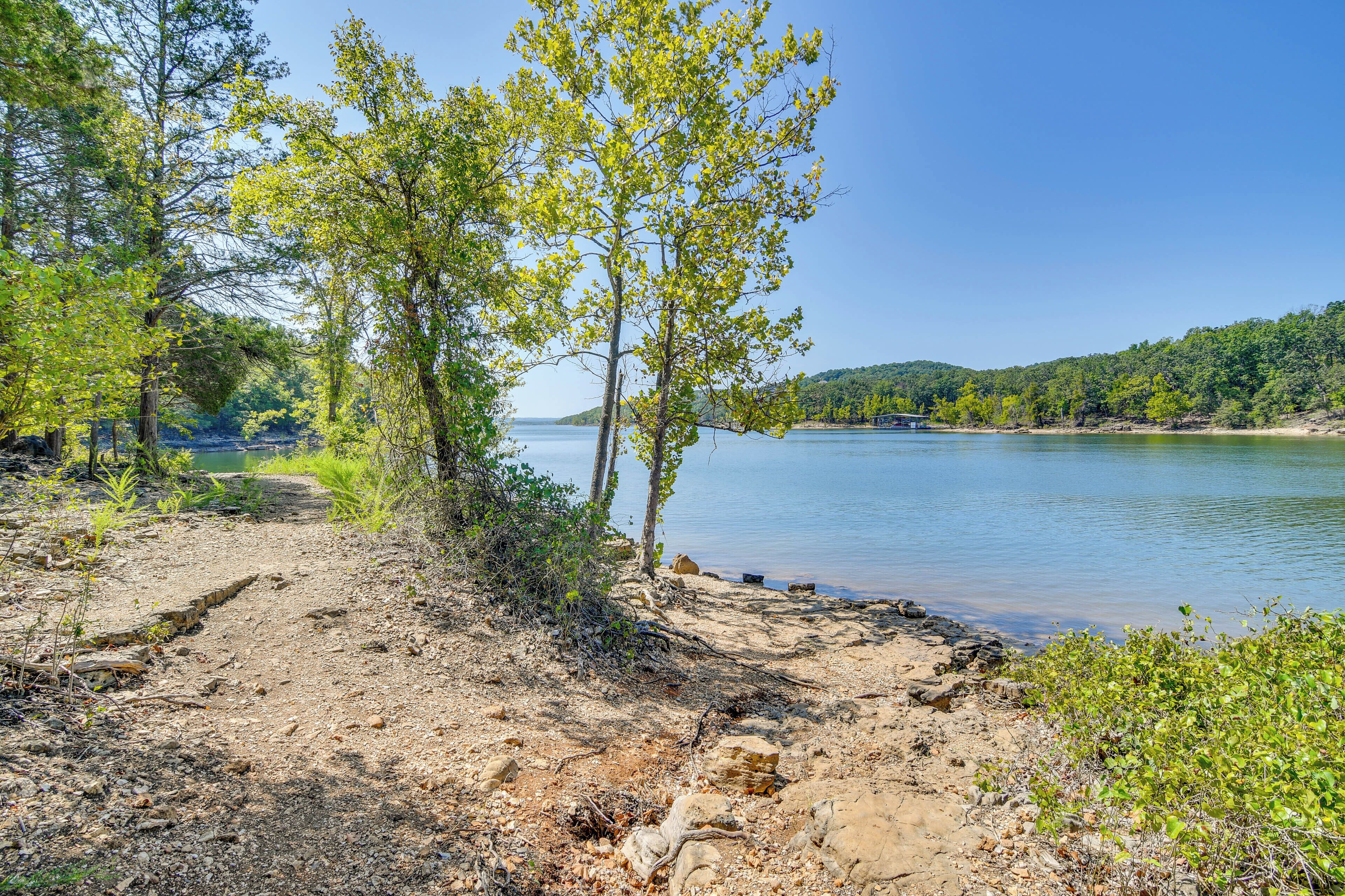 A natural landscape with a dirt path leading to a body of water, surrounded by trees and hills.