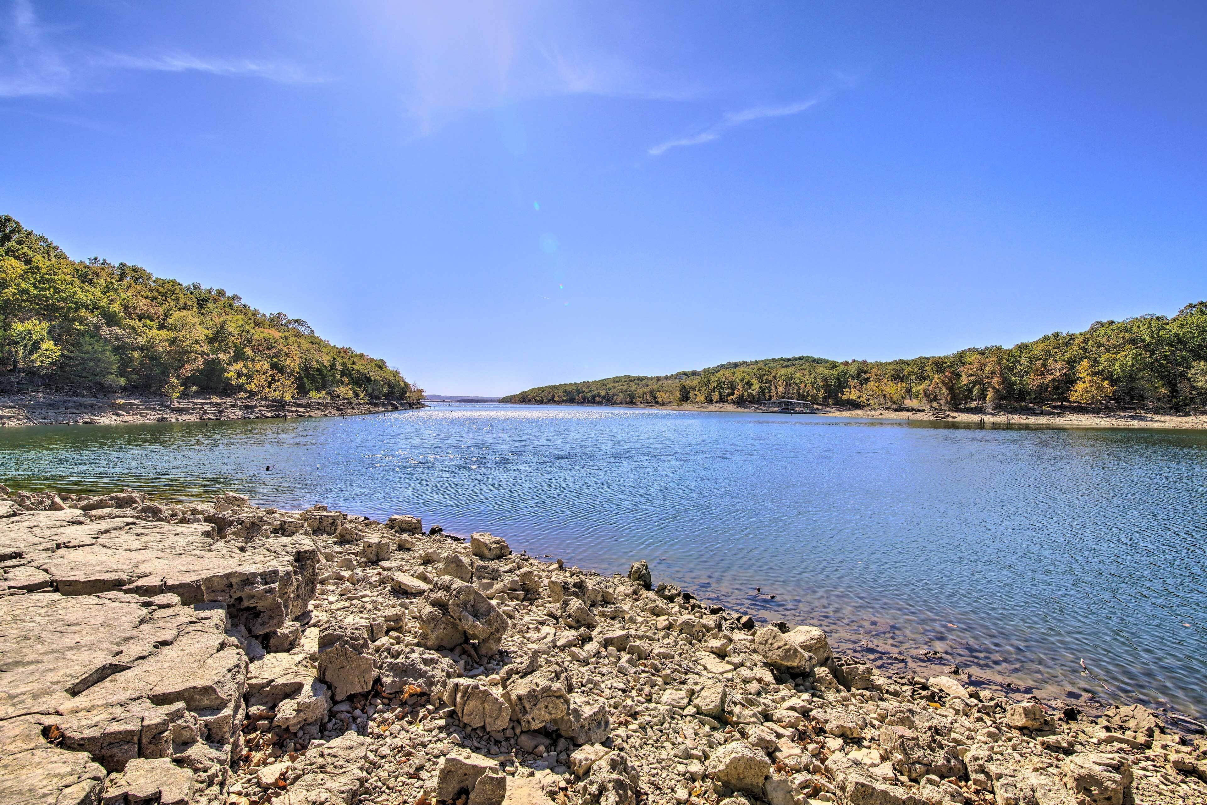 A rocky shoreline with a calm lake surrounded by forested hills.