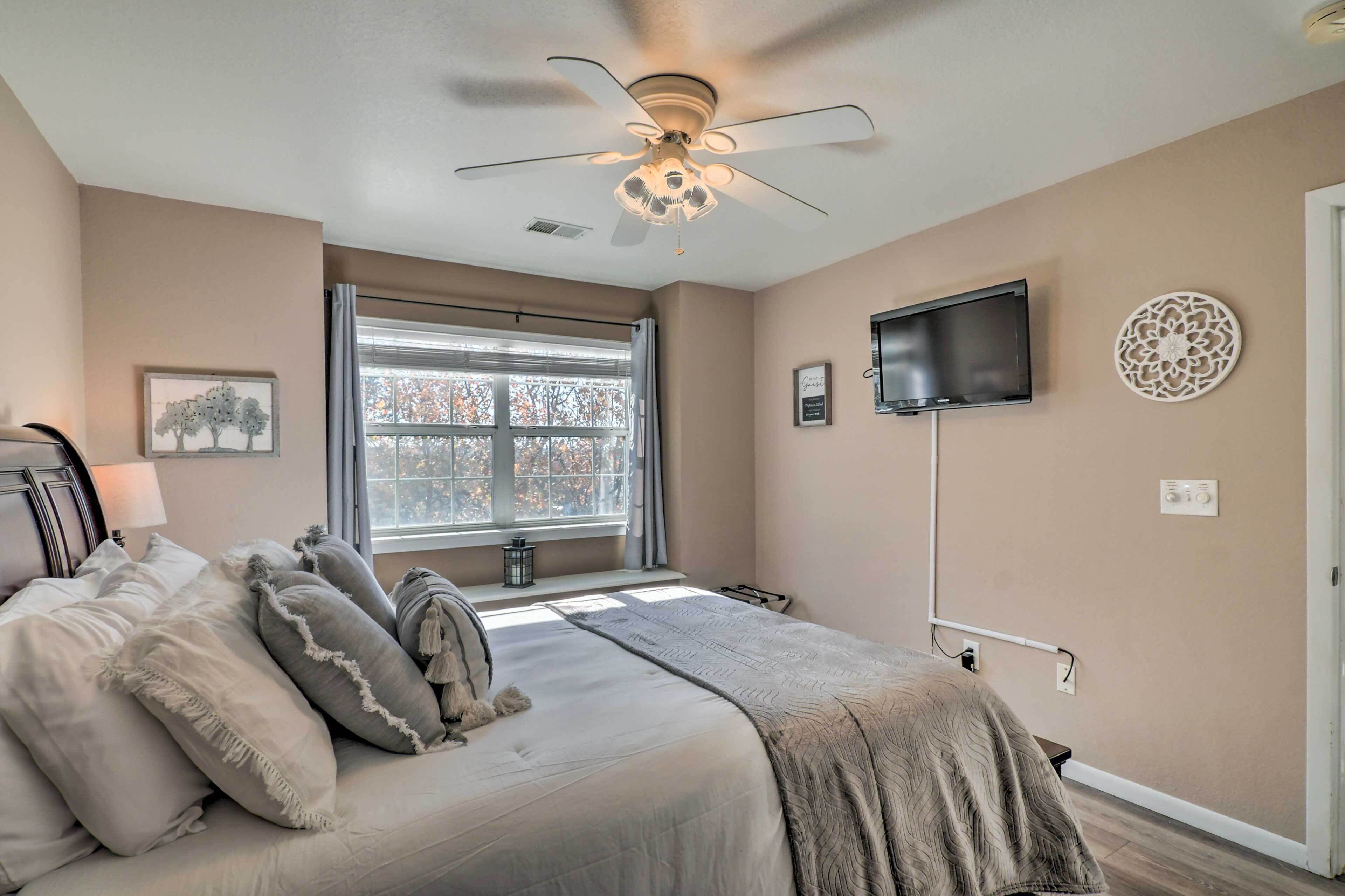 A bedroom with a bed, a ceiling fan, a TV, a window, and a wall-mounted decor piece.