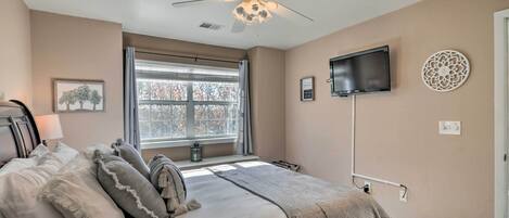 A bedroom with a bed, a ceiling fan, a TV, a window, and a wall-mounted decor piece.