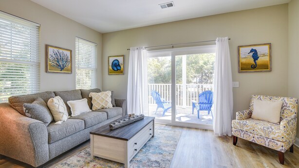 A living room with a sofa, armchair, coffee table, and a view to the outside.