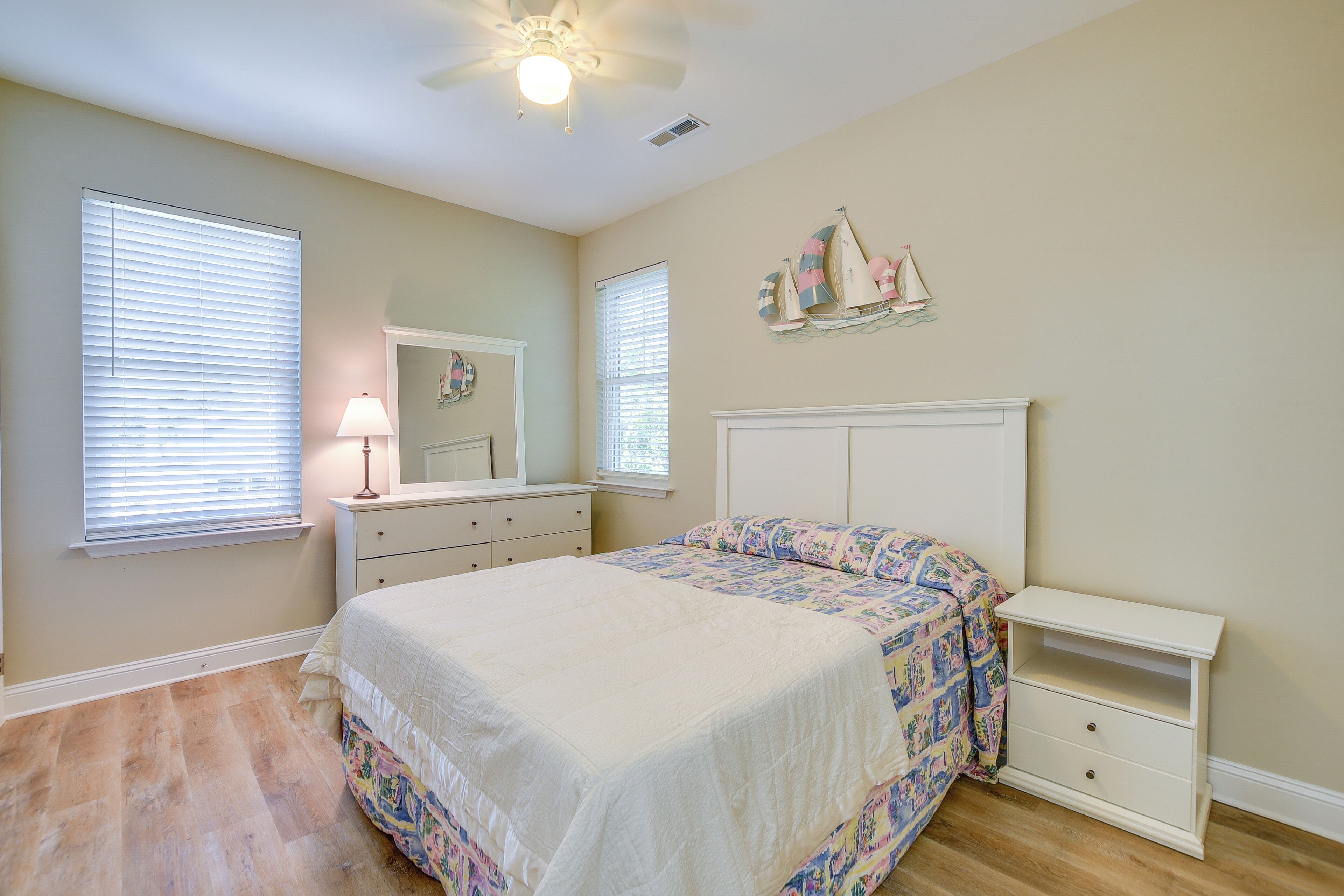 Quarto com cama, cômoda, mesa de cabeceira e ventoinha no teto.