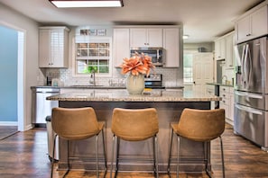 A modern kitchen with white cabinets, a granite countertop, a stainless steel refrigerator, and a vase with orange flowers on the island.
