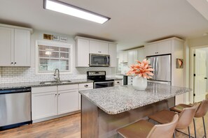A modern kitchen with white cabinetry, a granite countertop, stainless steel appliances, and a built-in island with bar stools. - Modern Home w/ Yard + Deck, 1 Mi to Clemson U! (Clemson)