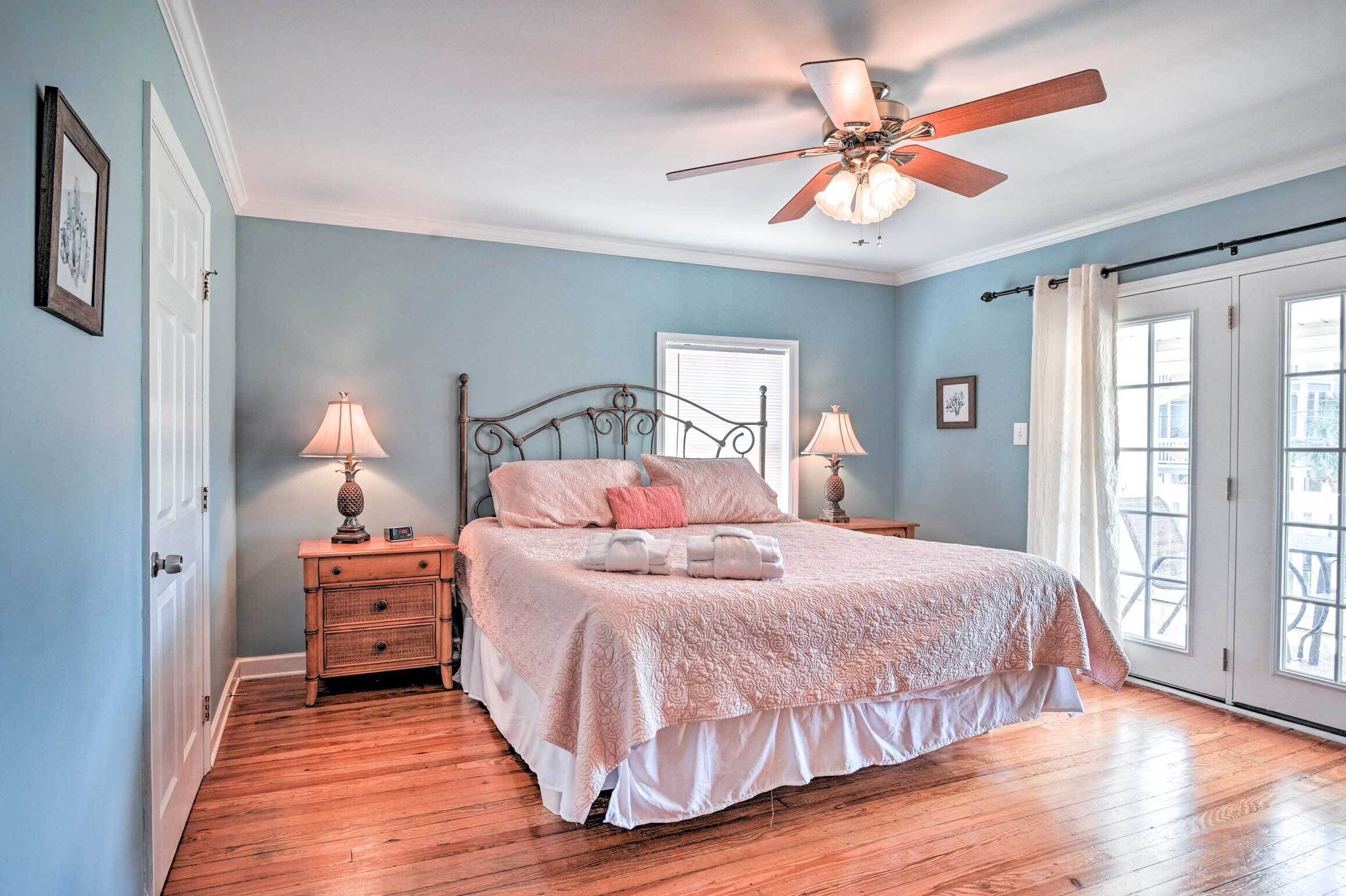 Une chambre à coucher comprenant un lit, deux tables de chevet, un ventilateur de plafond et une fenêtre avec des rideaux.
