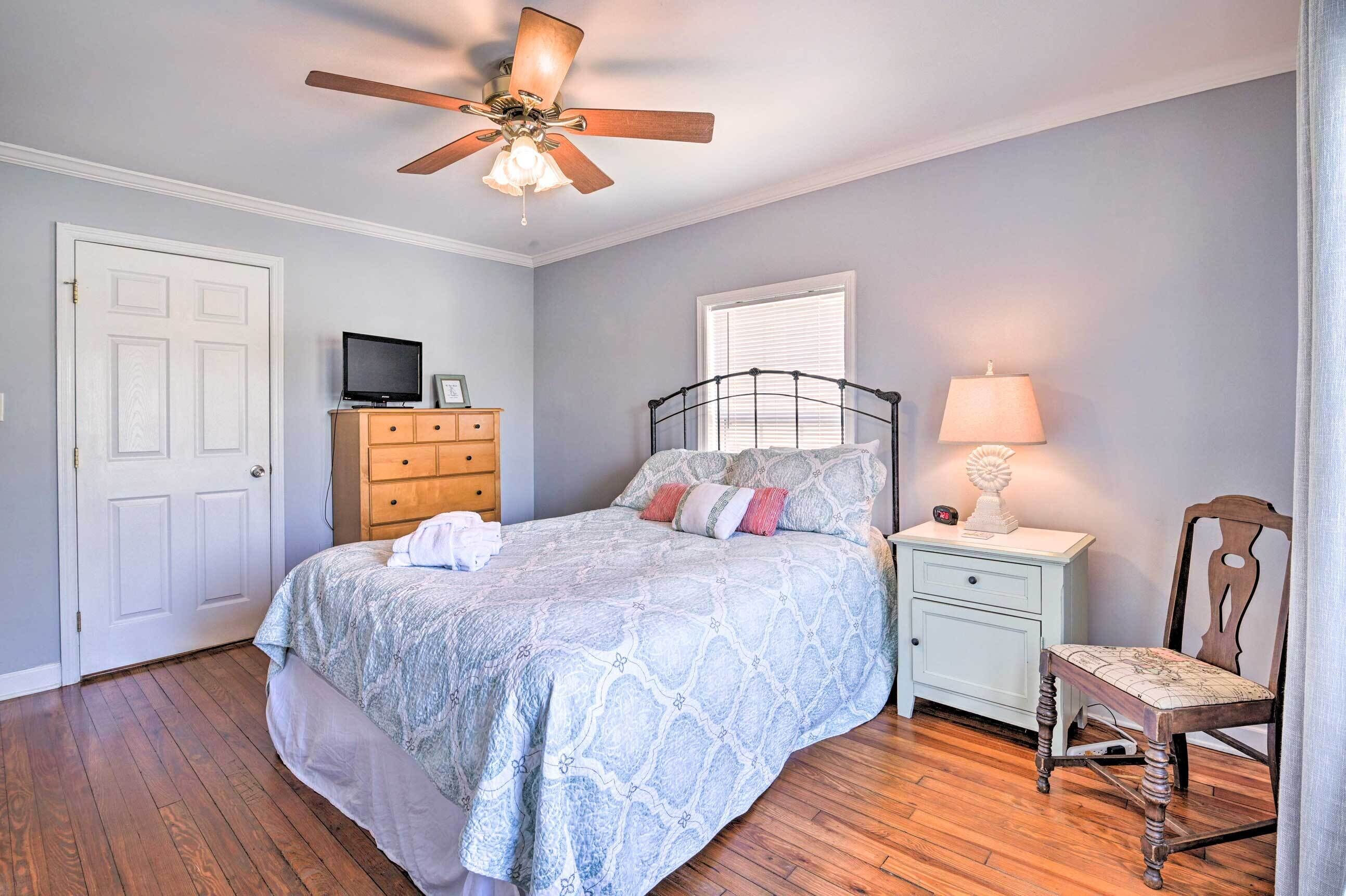 A bedroom with a bed, a nightstand, a chair, a dresser, a television, and a ceiling fan.