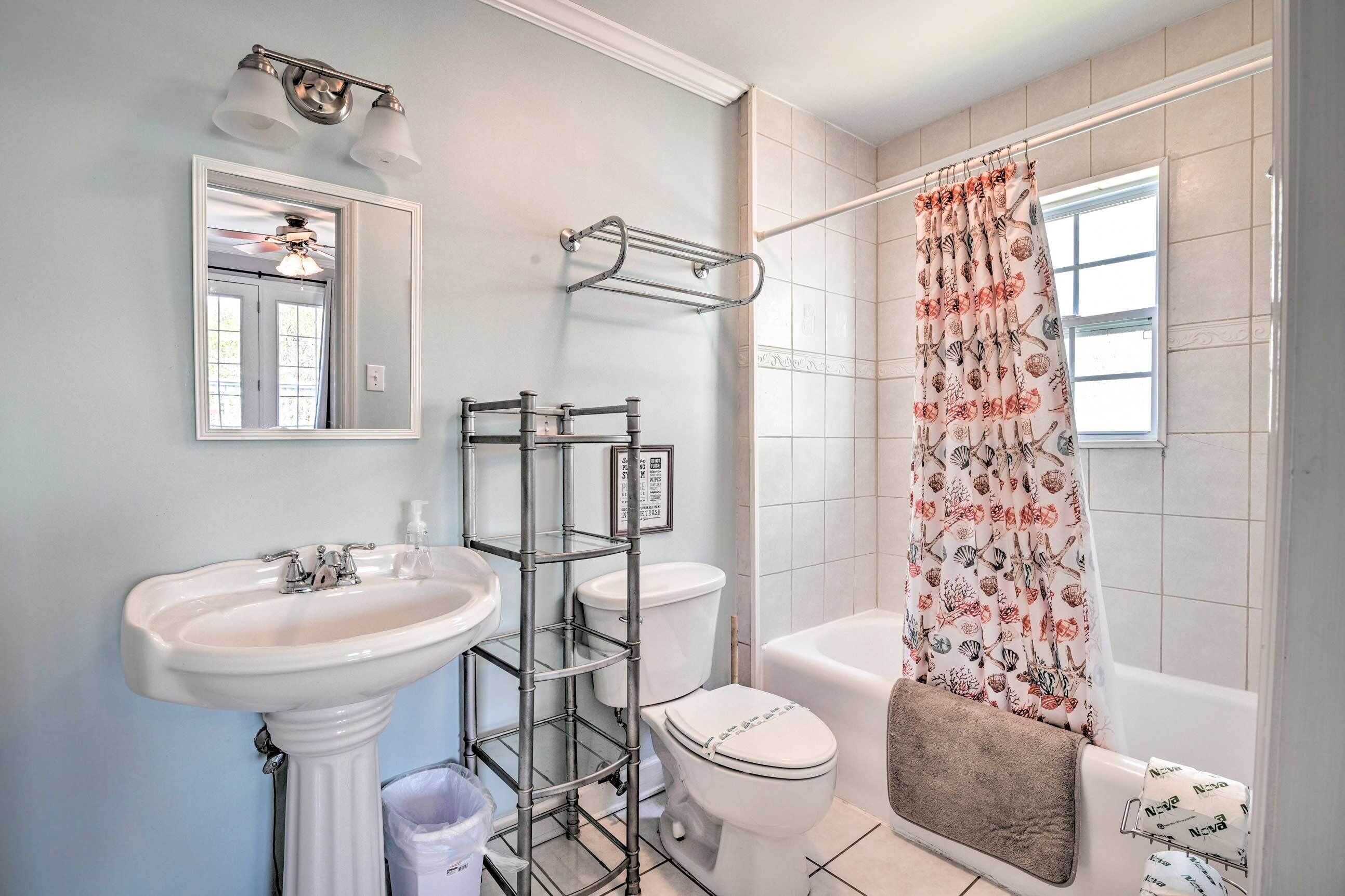 A bathroom with a pedestal sink, a toilet, a bathtub, and a shower curtain with a marine life pattern.