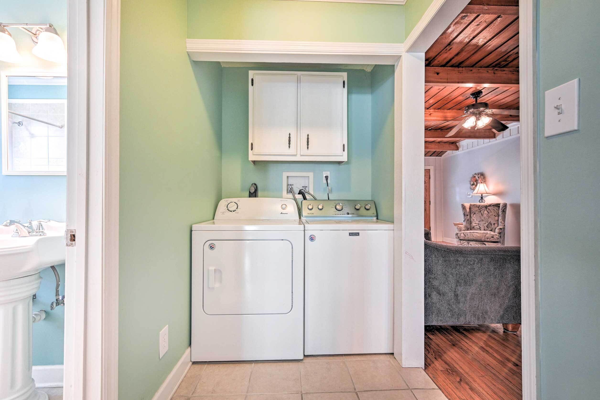 A laundry room with a washing machine and dryer, a cabinet above the dryer, and a chair in the adjacent room.