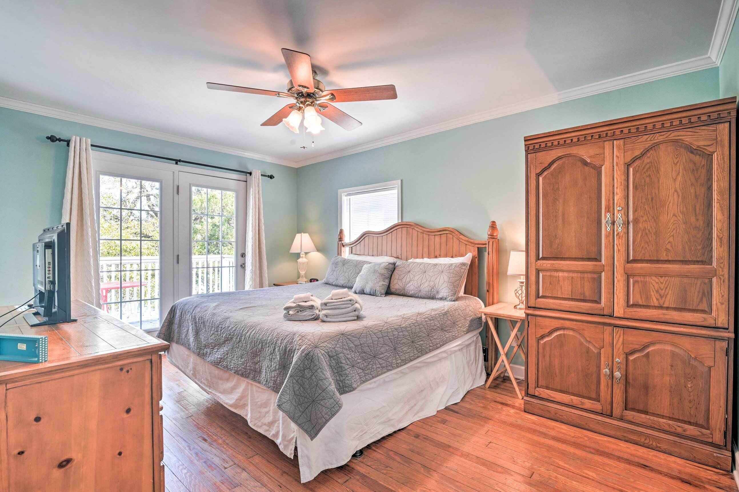 A bedroom with a bed, wooden wardrobe, ceiling fan, and a window with curtains.