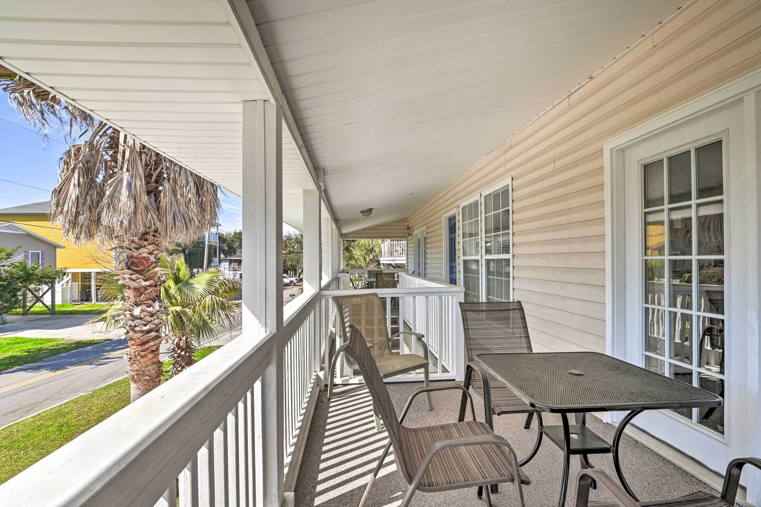 A covered porch with a table and chairs, a palm tree, and a view of the street.