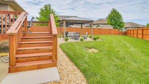 Un patio trasero con una escalera de madera, un porche cubierto con mobiliario exterior y un césped bien cuidado.