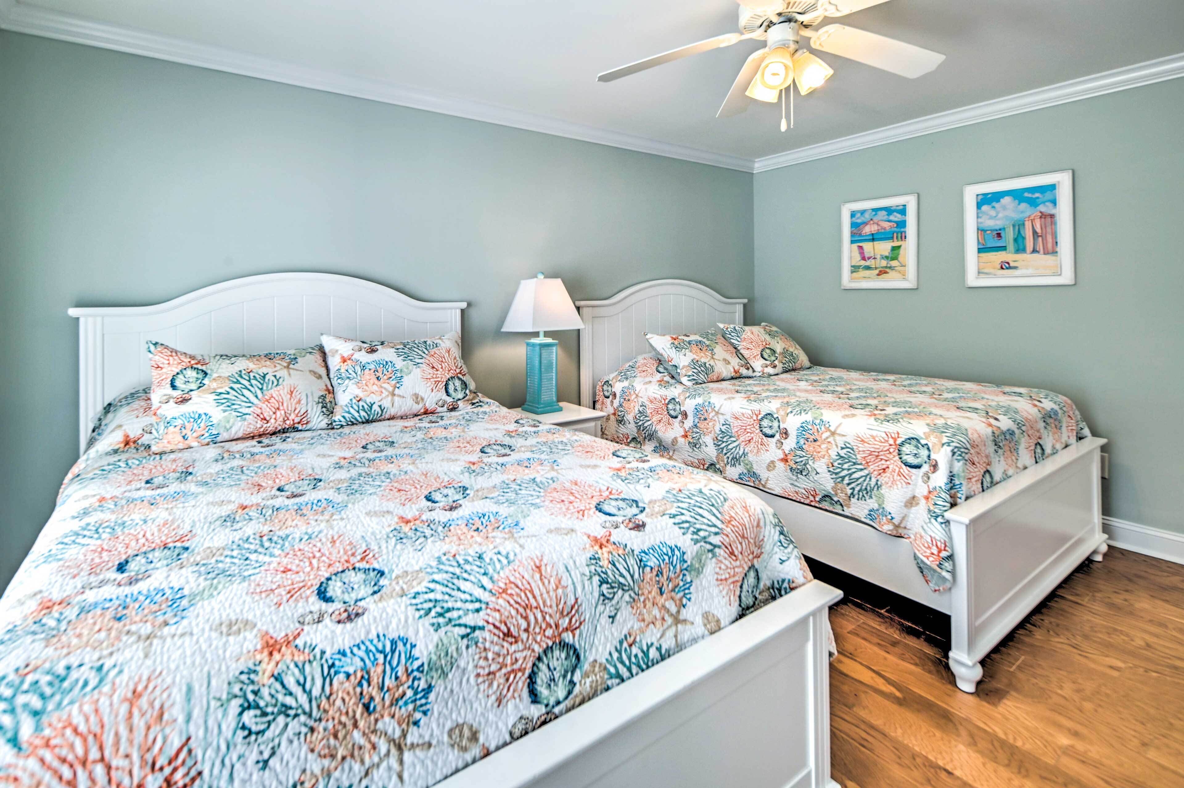 A bedroom with two beds, a ceiling fan, and two framed pictures on the wall.