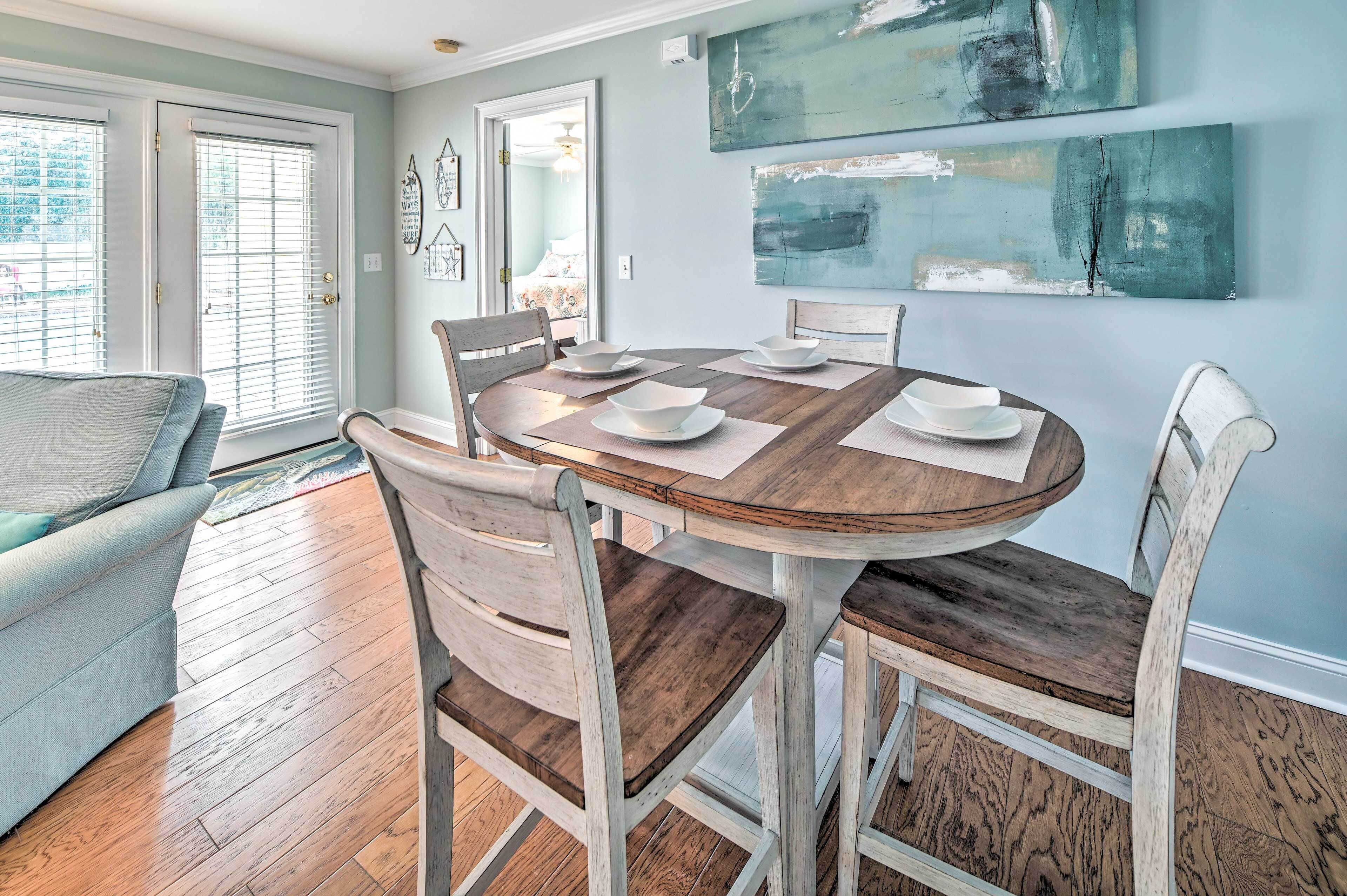 A dining area with a round wooden table, white chairs, and a light blue wall with abstract art.
