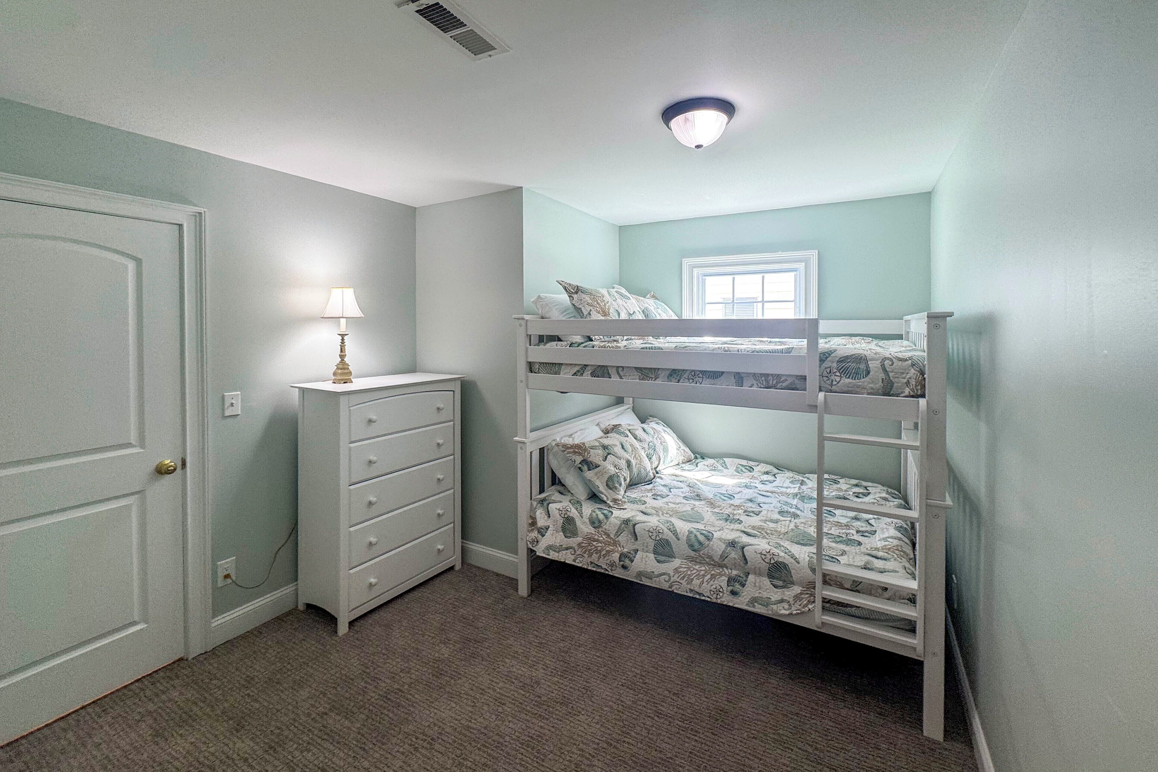 Een kamer met een stapelbed, een dressoir, een lamp en een raam.