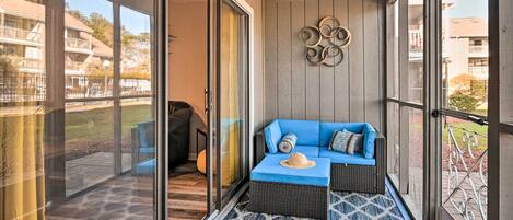 A balcony with a blue sofa, wicker furniture, and a patterned rug.