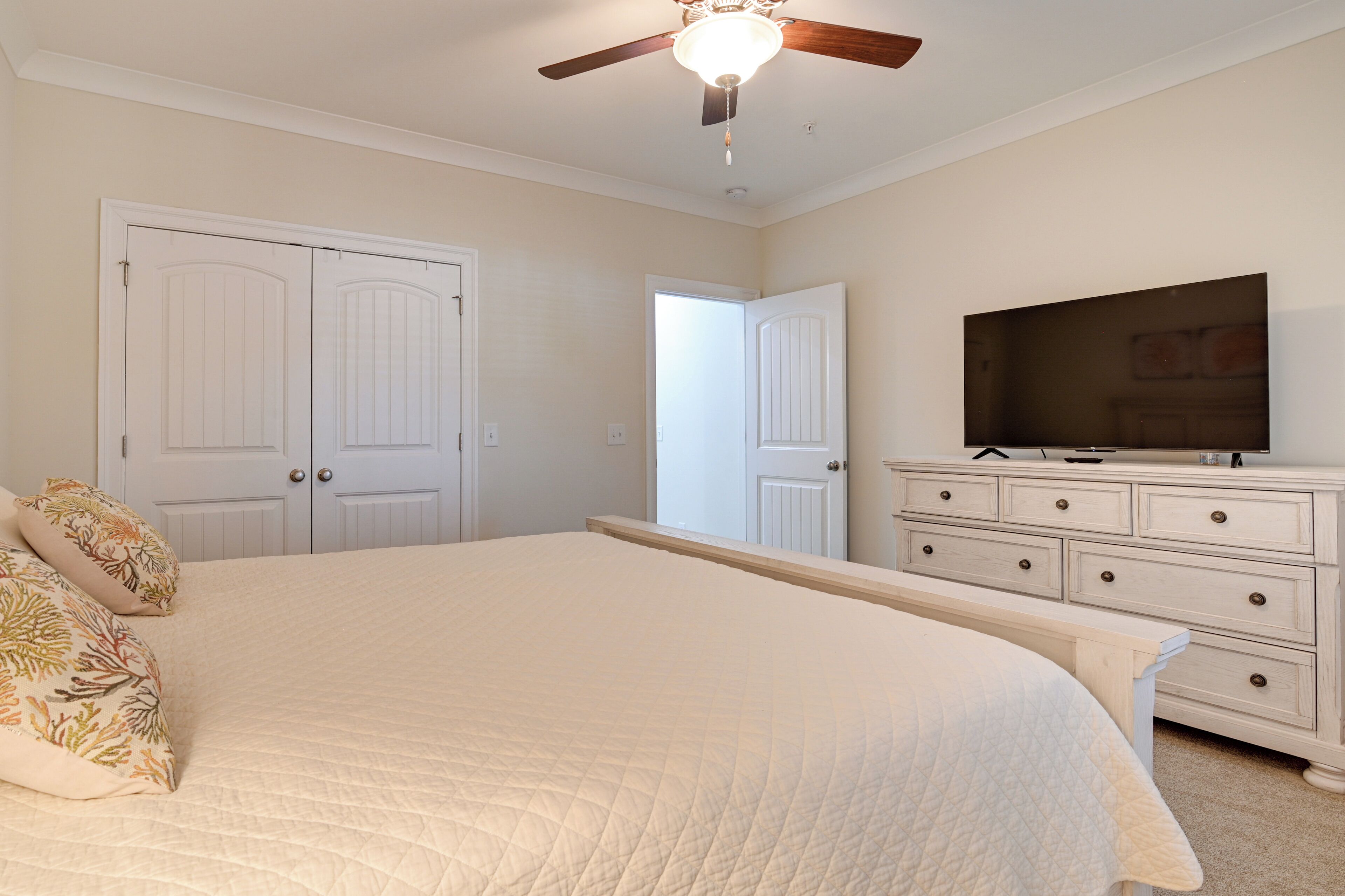 A bedroom with a large bed, a ceiling fan, a dresser, and a television.