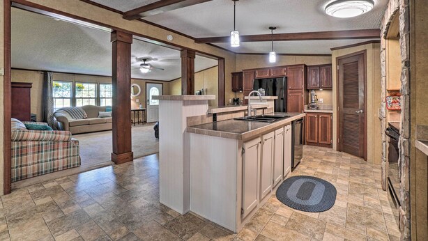 A spacious living area with a large sofa and a kitchen with wooden cabinets and a central island. - Monett Family Ranch Home w/ Fireplace & Huge Deck! (Purdy)