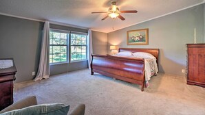A bedroom with a large bed, a ceiling fan, a window with curtains, a wooden dresser, and a painting on the wall. - Monett Family Ranch Home w/ Fireplace & Huge Deck! (Purdy)