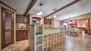 A spacious kitchen with wooden cabinets, a stone backsplash, and a bar area with stools. - Monett Family Ranch Home w/ Fireplace & Huge Deck! (Purdy)