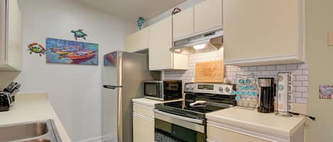 A compact kitchen with a refrigerator, microwave, stove, and oven. There are wall decorations and a sink with a patterned backsplash.