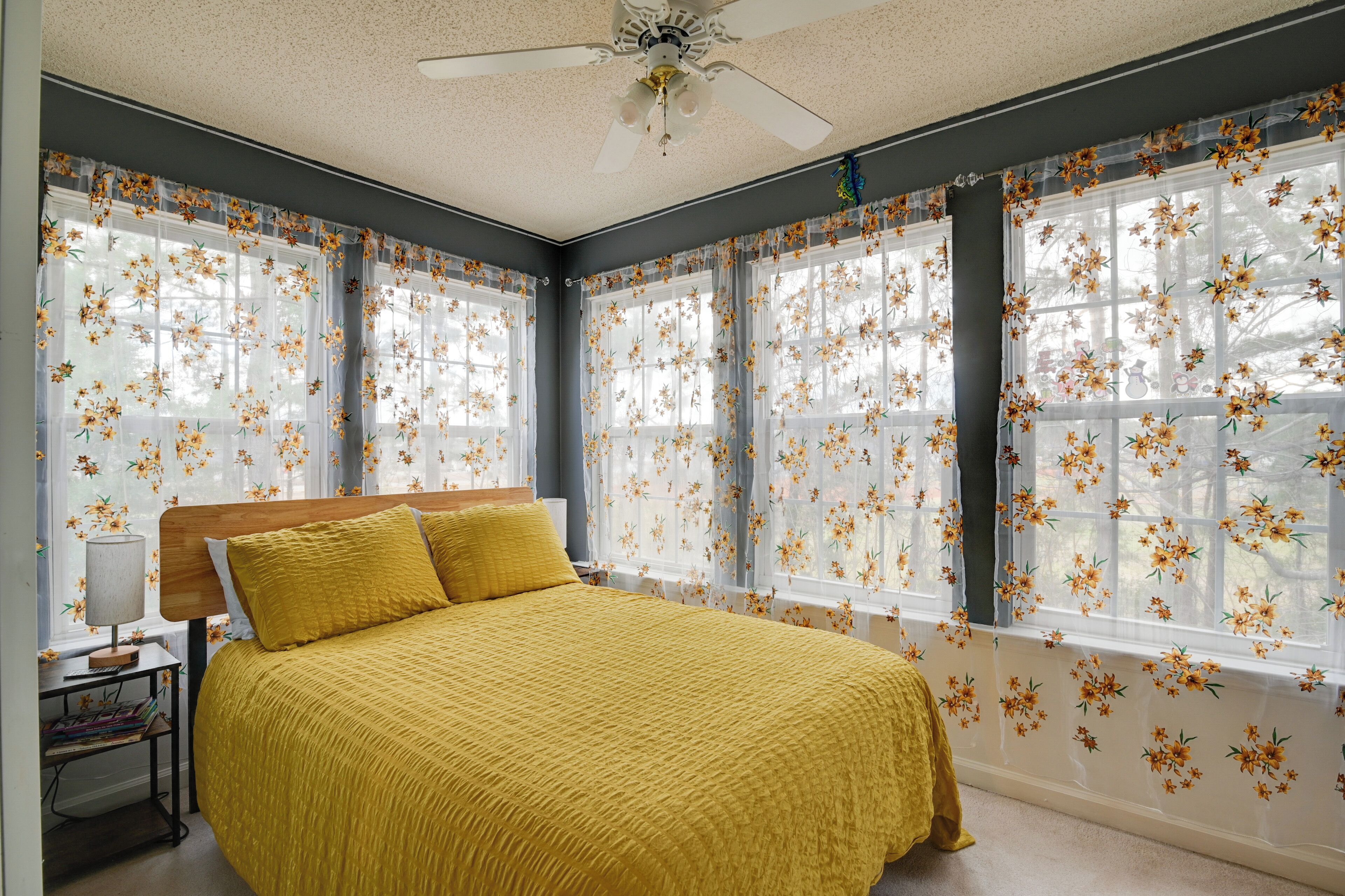 A bedroom with a bed, a nightstand, a lamp, and floral curtains.