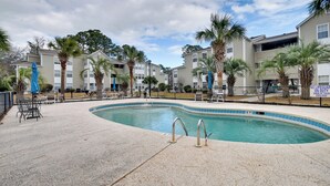A swimming pool with a tiled edge, surrounded by lounge chairs and umbrellas, with apartment buildings in the background. - Myrtle Beach Condo 2 Mi to Surfside Beach! (Surfside Beach)