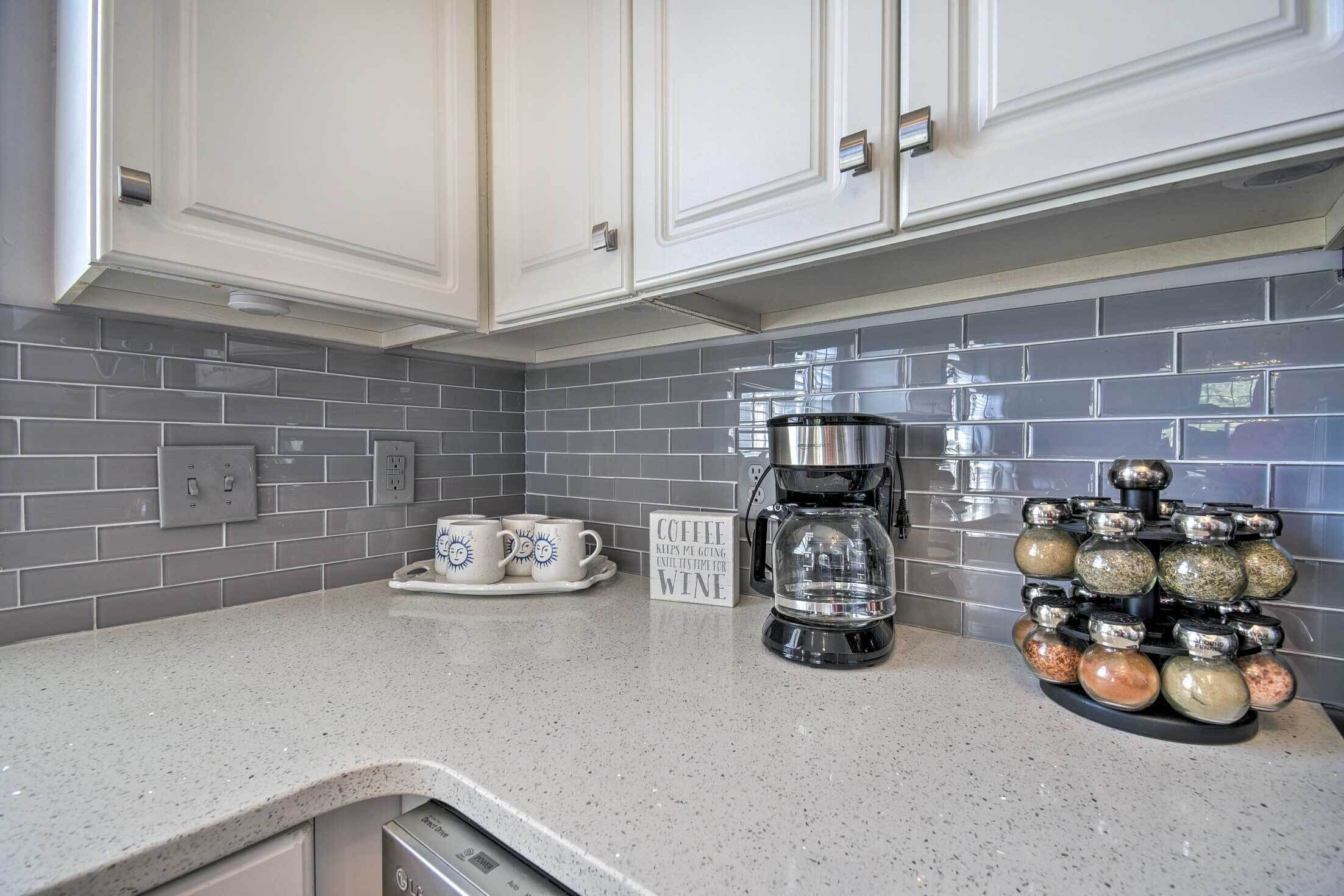 A kitchen with white cabinets, grey tiled backsplash, a coffee maker, and a spice rack.
