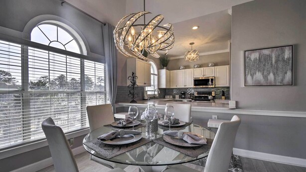 Un espace repas moderne avec une table en verre, des chaises blanches et un lustre décoratif.