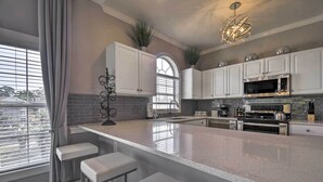 Une cuisine moderne avec des meubles blancs, un grand îlot central doté de tabourets, un four à micro-ondes en acier inoxydable et une cuisinière à gaz.