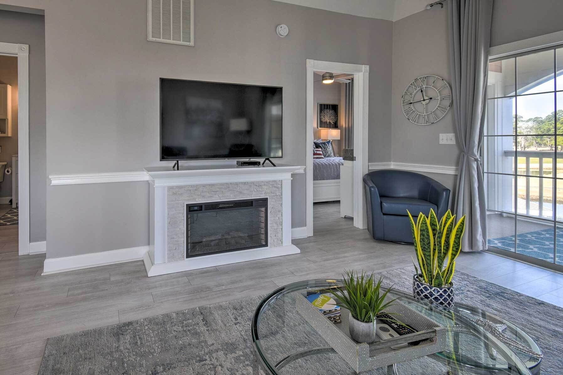 A modern living room with a fireplace, a flat-screen TV, a comfortable seating area, and a large window with curtains.