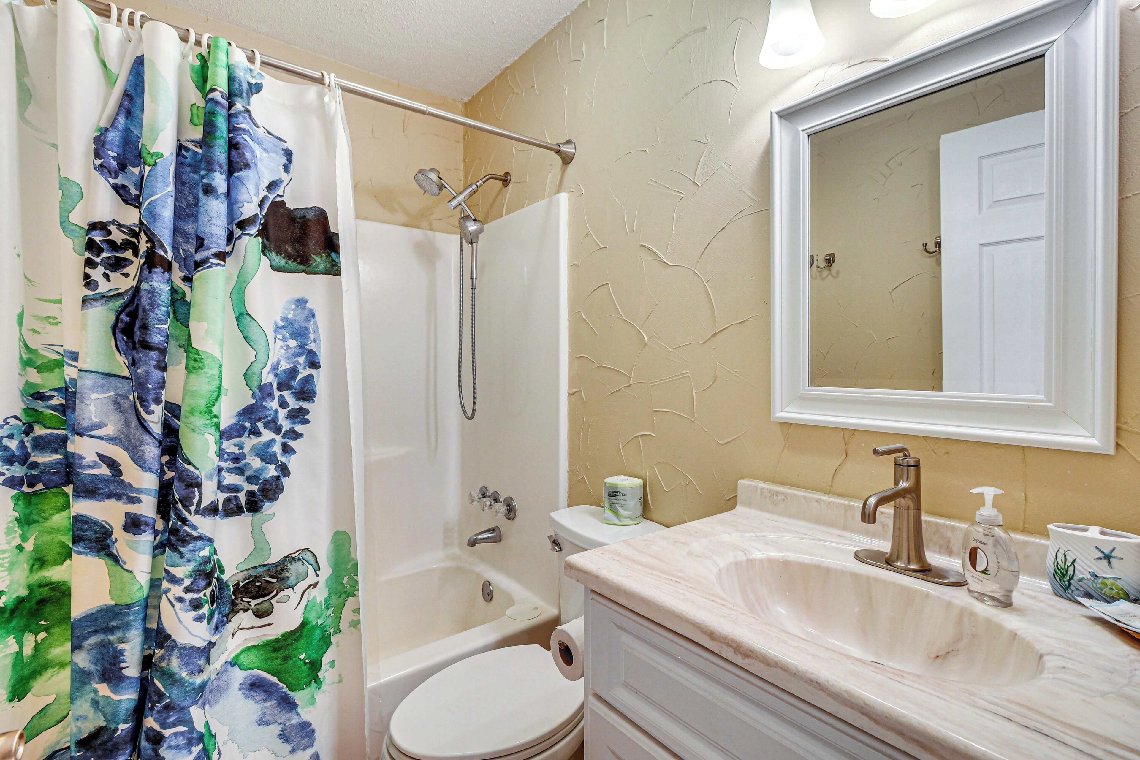 A bathroom with a shower, toilet, sink, and mirror.