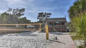 A beach volleyball court with a wooden boardwalk leading to a building with a balcony. - Walk to Beach: Nautical Hilton Head Resort Condo! (Hilton Head Island)