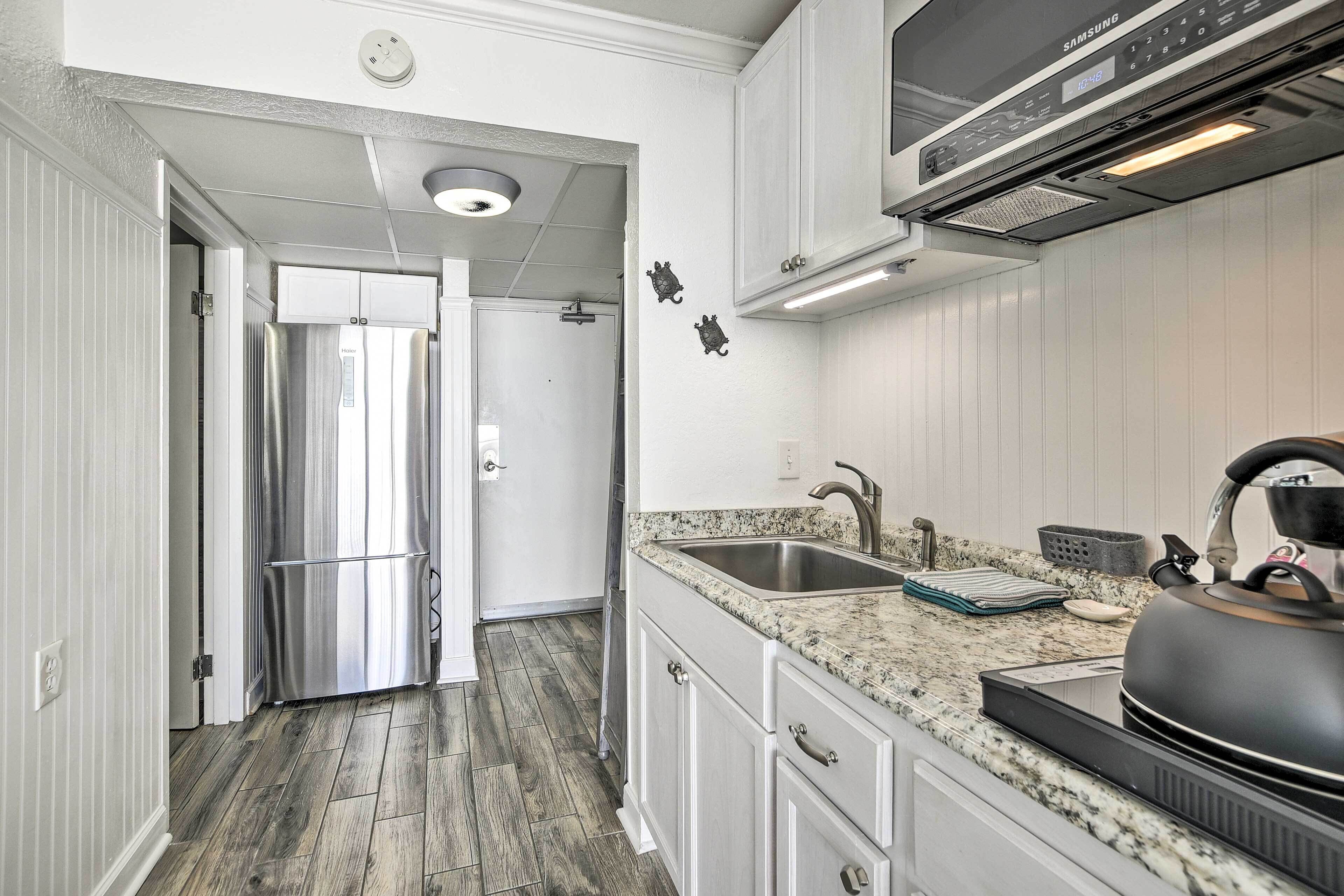A kitchen with a stainless steel refrigerator, a microwave, a kettle, and a granite countertop.