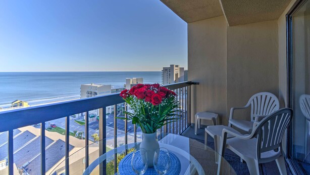 A balcony with a table, chairs, and a vase of flowers overlooking the ocean. - Walk to Ocean: Myrtle Beach Condo w/ Views! (Myrtle Beach)