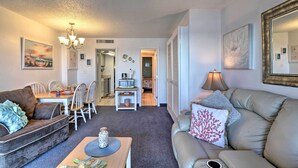 A living room with a sofa, a coffee table, and a dining area with chairs and a table. - Walk to Ocean: Myrtle Beach Condo w/ Views! (Myrtle Beach)