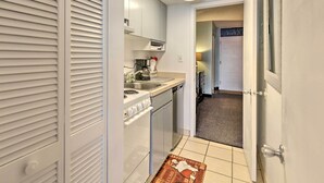A compact kitchen with a stove, sink, and dishwasher. A small rug with a kitchen theme is on the floor. - Walk to Ocean: Myrtle Beach Condo w/ Views! (Myrtle Beach)