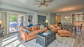 Ein geräumiges Wohnzimmer mit Deckenventilator, einem Glastisch, Ledersofas und einem Essbereich mit einer Kronleuchter.