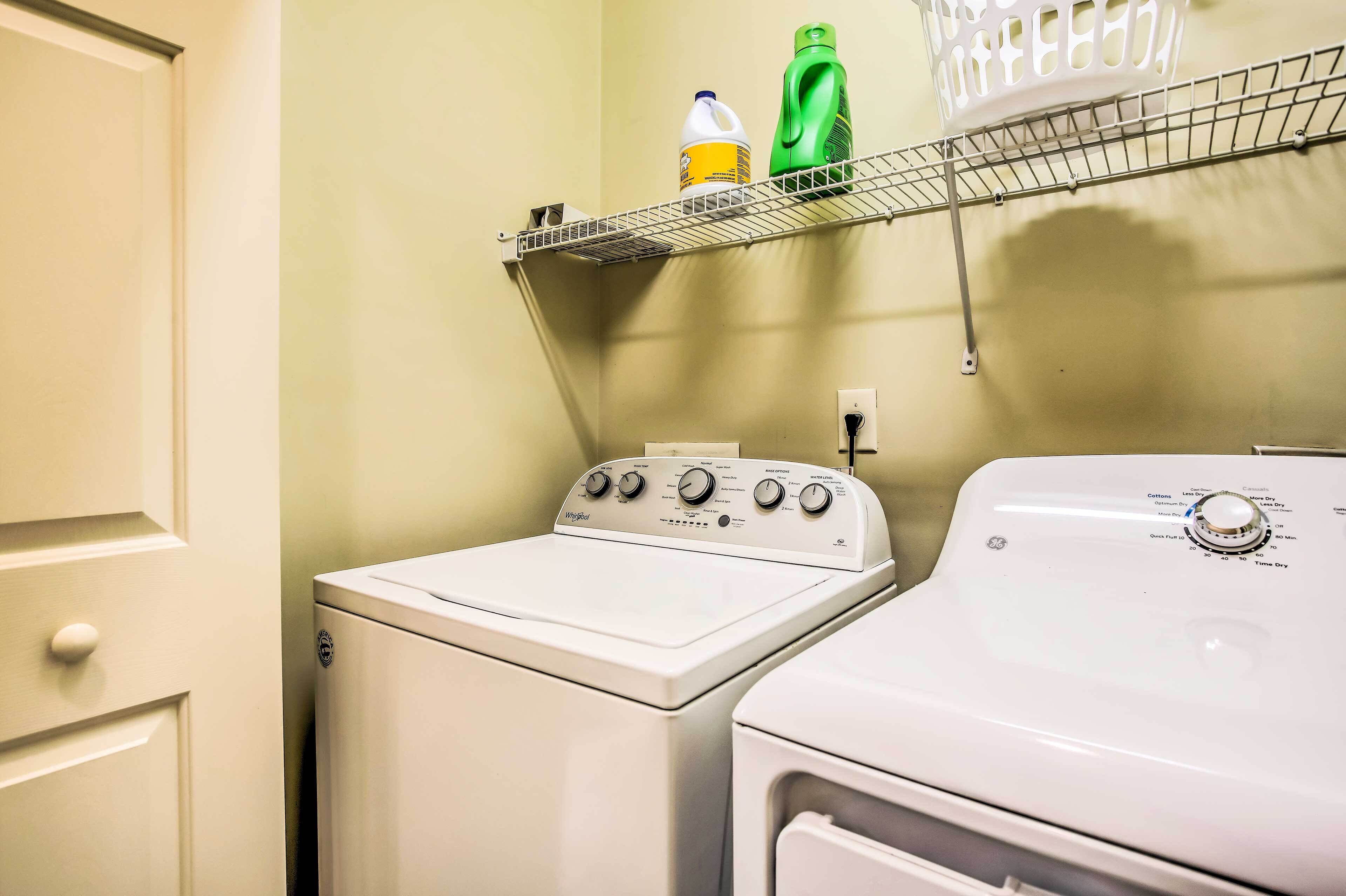 Un espace buanderie comprenant un lave-linge et un sèche-linge à chargement frontal, une étagère avec des produits de nettoyage et une caméra de surveillance fixée au mur.