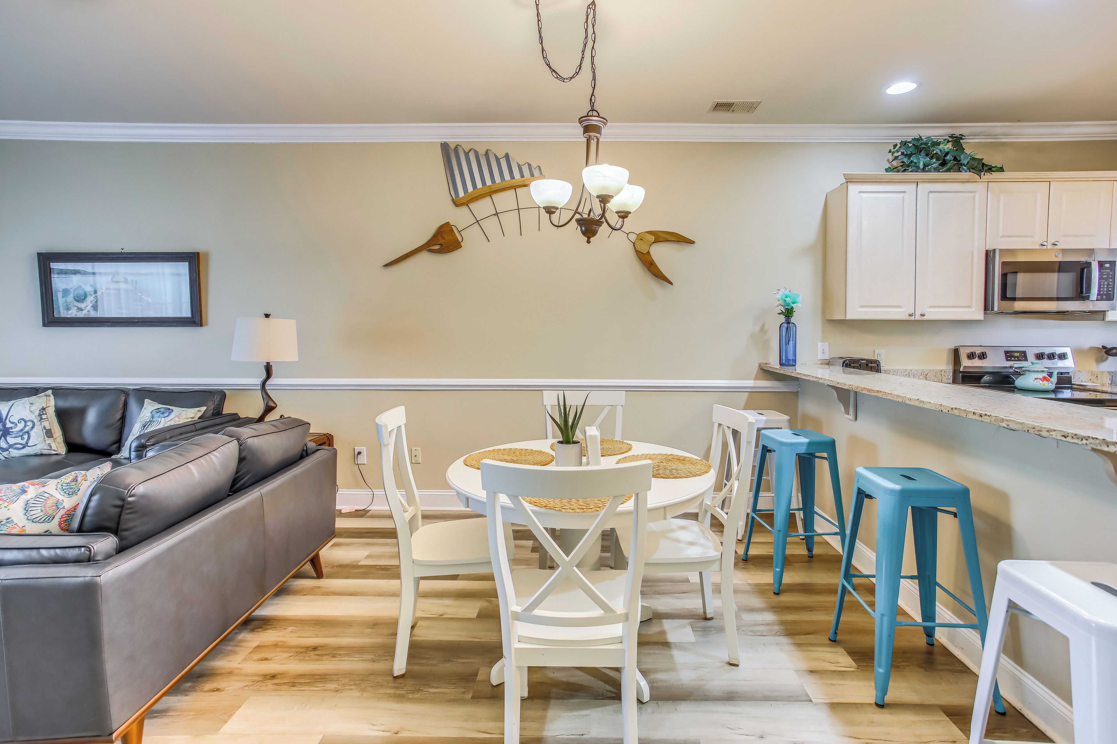 A modern kitchen with white cabinets, a central island with stools, and a dining table with chairs.