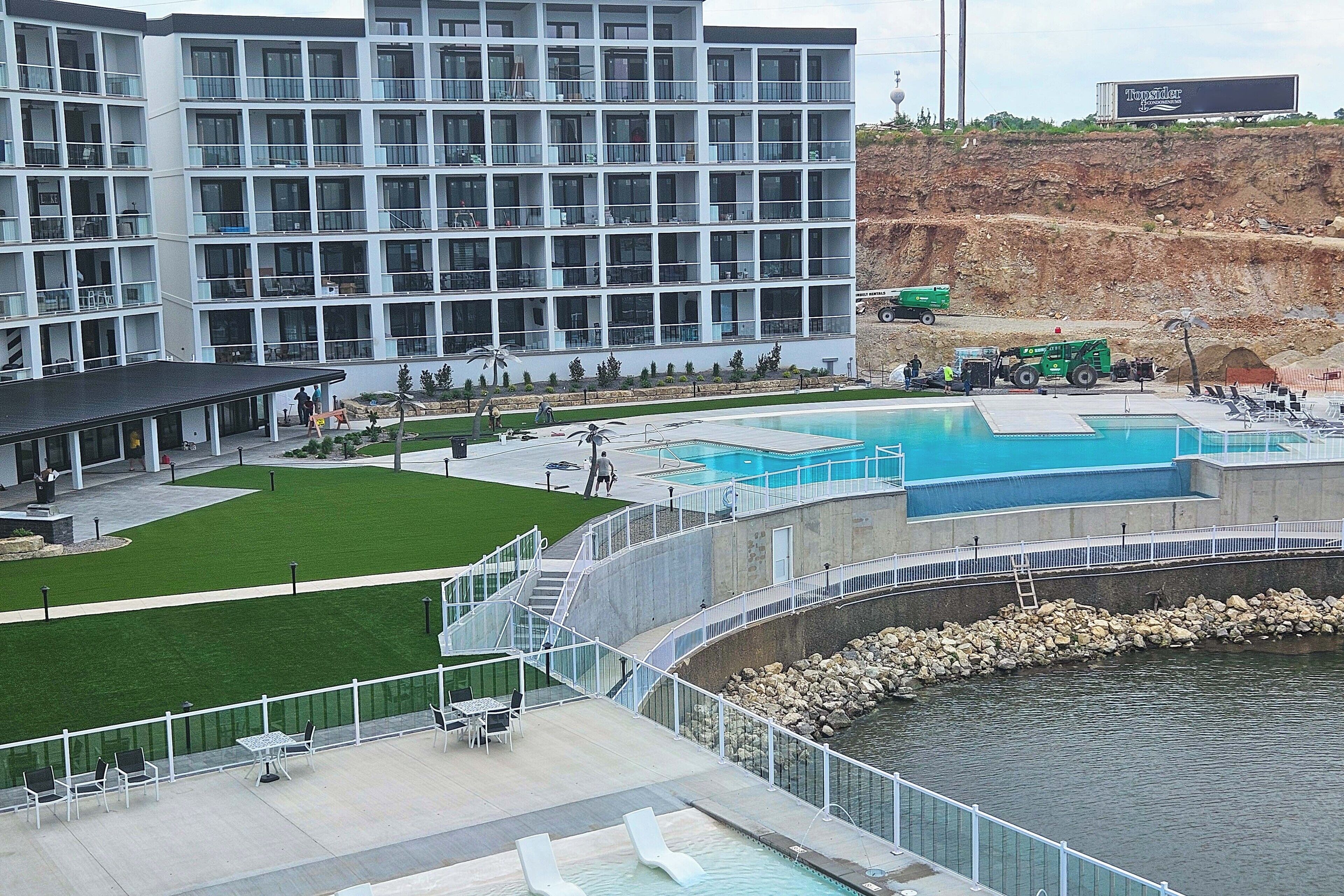 A modern hotel with multiple balconies, a swimming pool, and a landscaped area.