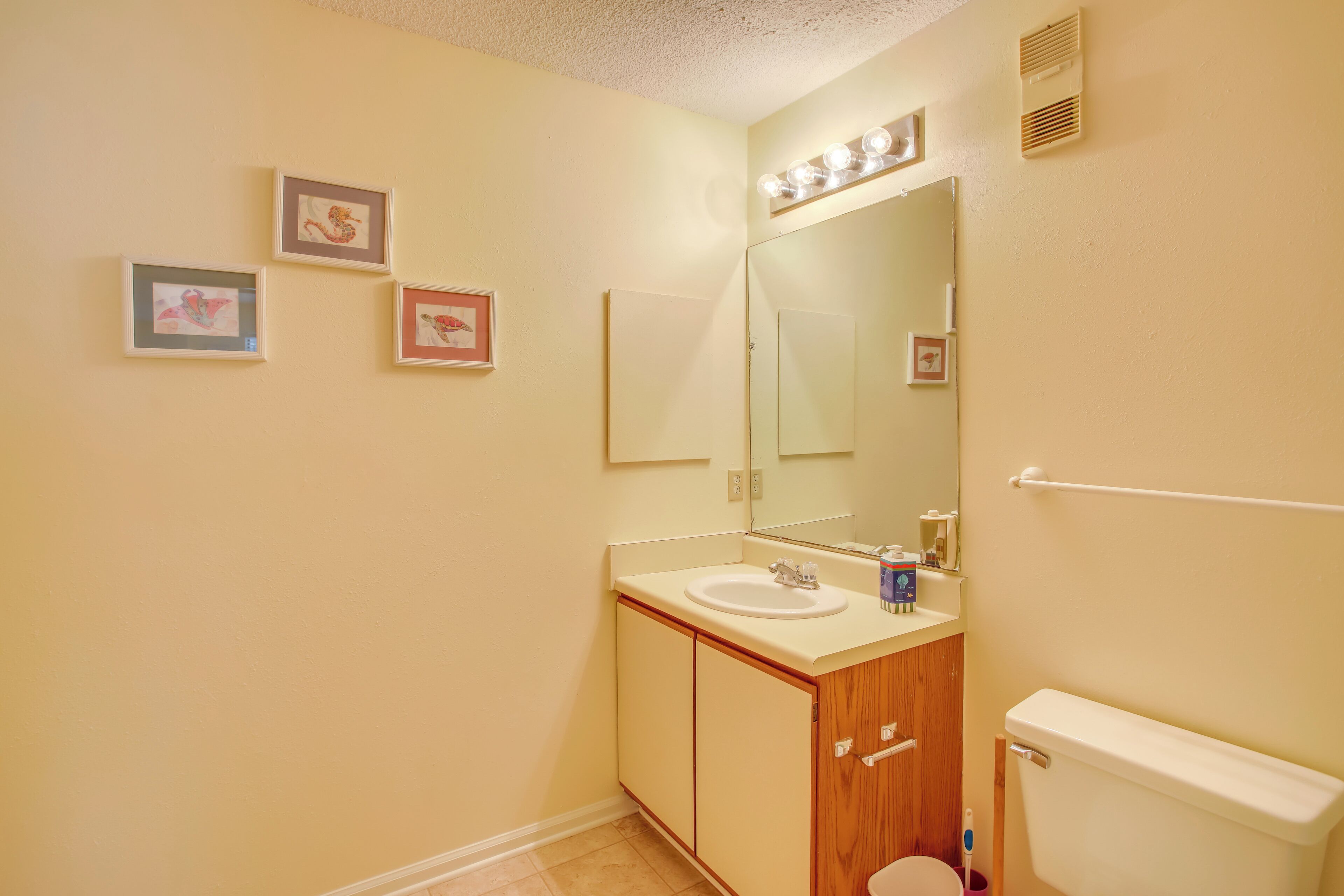 A bathroom with a sink, mirror, toilet, and framed pictures on the wall.
