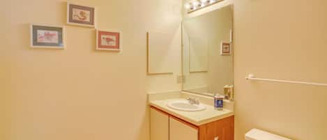 A bathroom with a sink, mirror, toilet, and framed pictures on the wall.