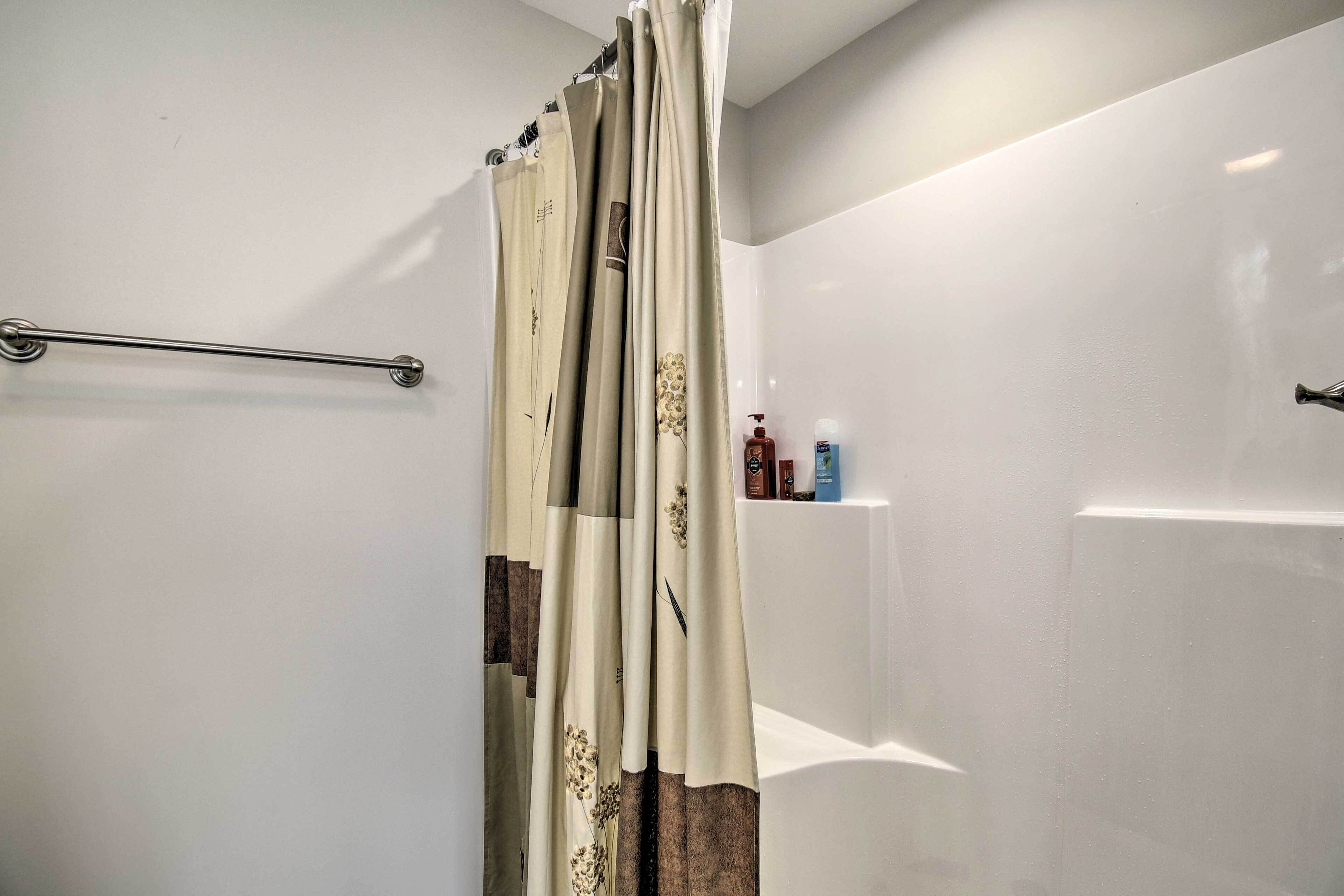 Ein Badezimmer mit Duschvorhang, Handtuchhalter und Pflegeprodukten auf einem Regal.