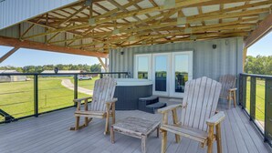 A covered outdoor deck with wooden chairs and a table, a hot tub, and a view of a golf course. - One-of-a-kind Container Home on Mount Vernon Farm! (Mount Vernon)