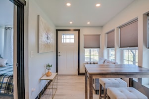 Una habitación moderna con una mesa de comedor de madera, un banco, una puerta y una ventana con persianas.